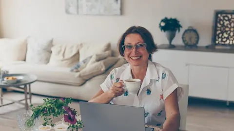 Older woman drinking coffee and smiling in house in white shirt during daytime . .