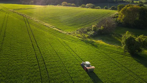 Aerial view on agricultural landscape in spring. A farmer with his machine is driving on a wheat field. Captured with a drone in southern Germany.