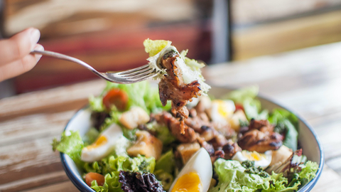 A high-angle close-up view of a salad in a bowl on the wooden table in a restaurant during daytime